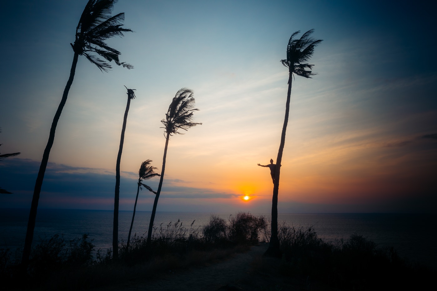 Senggigi Beach: An Honest Guide to Lombok's Old Hub 3 Sunset over the Lombok Strait seen through palms from Malimbu on the Senggigi coast road