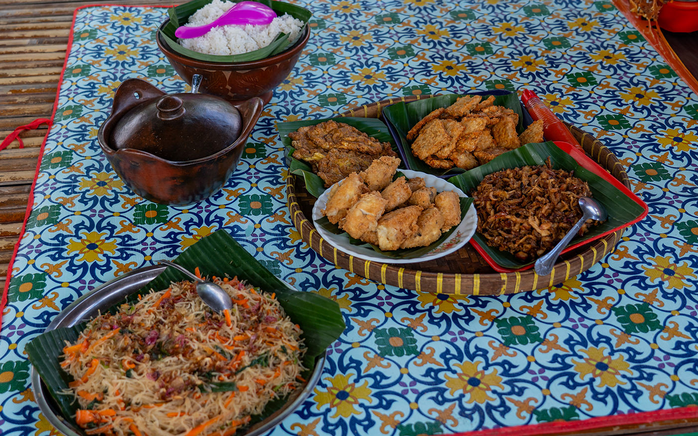 Sasak food plates of sate, rice, sambal and fried snacks laid out on a patterned cloth in Lombok
