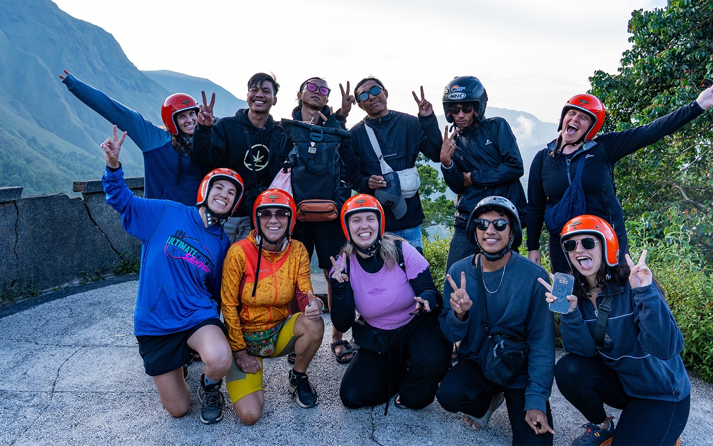 Lombok Loop group in helmets and riding jackets with arms raised on a road trip in Lombok