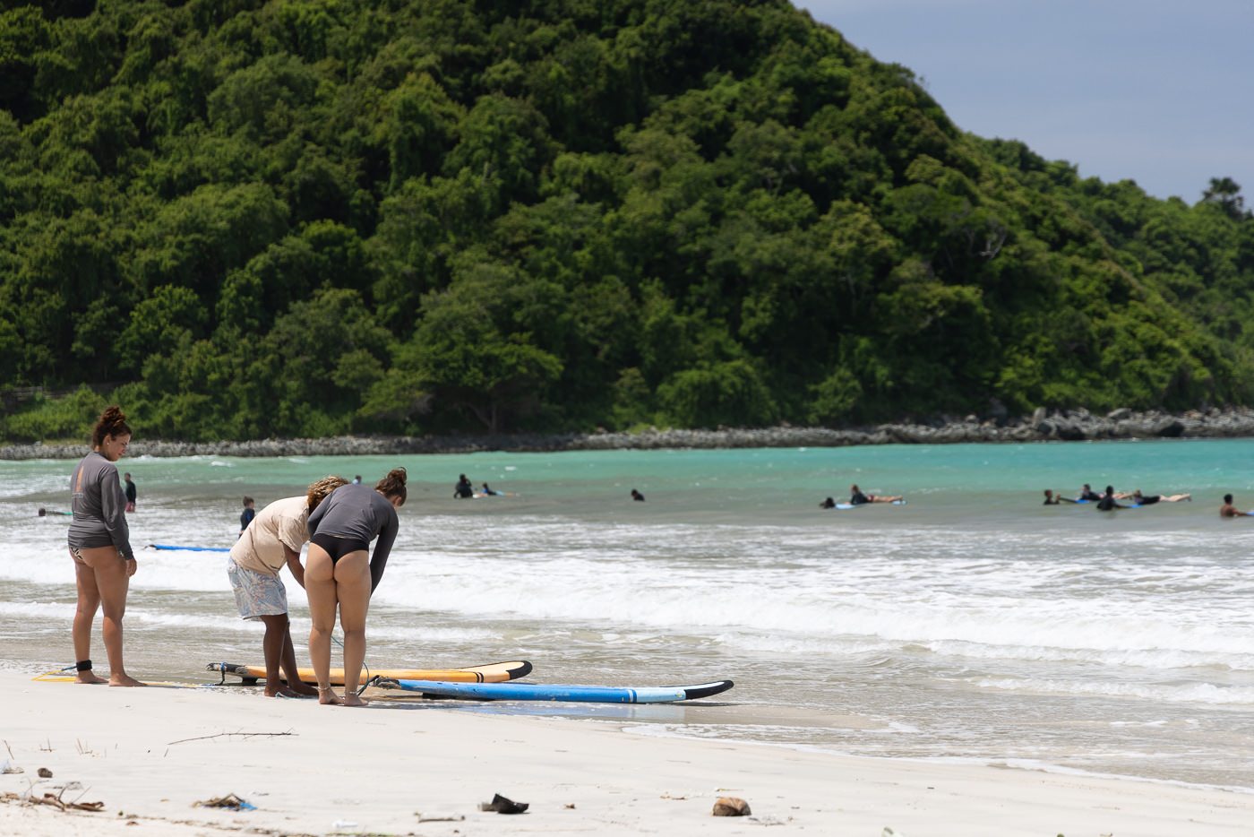 Beginner surfers standing on the sand at Selong Belanak Beach with boards and surfers in the whitewater behind