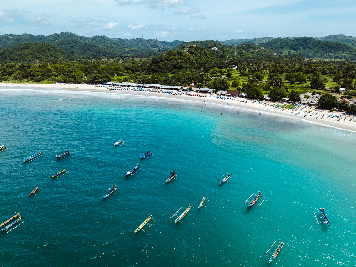 Aerial view of Selong Belanak Beach in south Lombok with surf school warungs along the sand and outrigger boats offshore